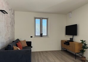 Ein Wohnzimmer mit einem dunkelgrauen Sofa, einem Holzschrank und einem an der Wand befestigten Fernseher.