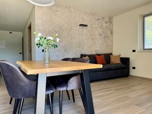 Een moderne woonruimte met een eettafel, stoelen, een bank en een decoratieve vaas met bloemen.