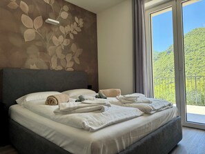 Ein Schlafzimmer mit Bett, Kissen und Handtüchern. Ein Fenster bietet Blick auf die grüne Umgebung.