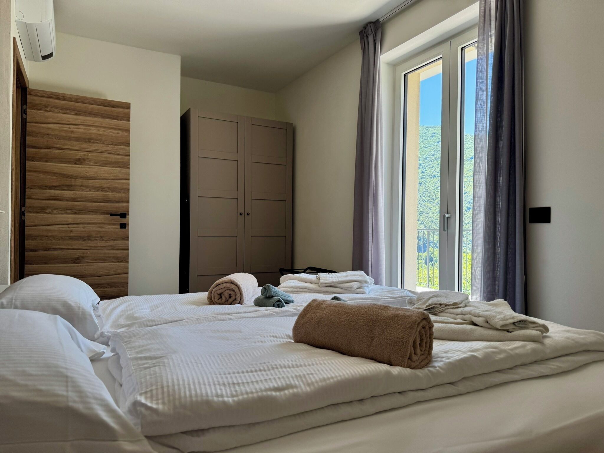 A hotel room with a bed, a wardrobe, and a window with curtains.