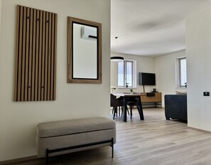 A modern living room with a bench, a dining area with a table and chairs, and a TV mounted on the wall.