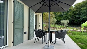 Eine Terrasse im Freien mit Tisch und Stühlen, einem großen Sonnenschirm und Blick auf einen Garten.