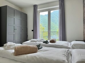 Habitación de hotel con dos camas, un armario y balcón con vista a la montaña.