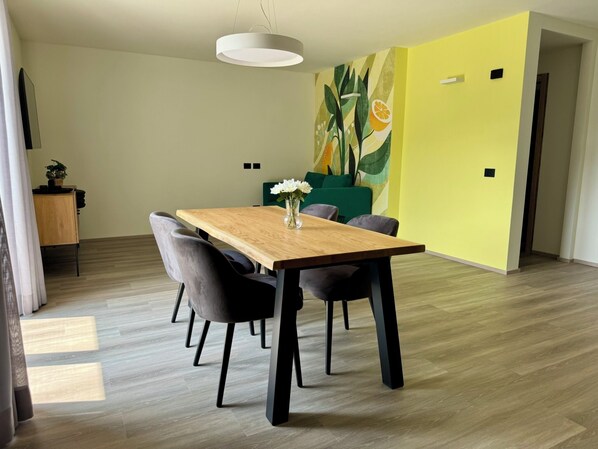 Ein Essbereich mit einem Holztisch, vier Stühlen, einer Vase mit Blumen sowie einer Wand mit Pflanzen- und Fruchtmotiv.