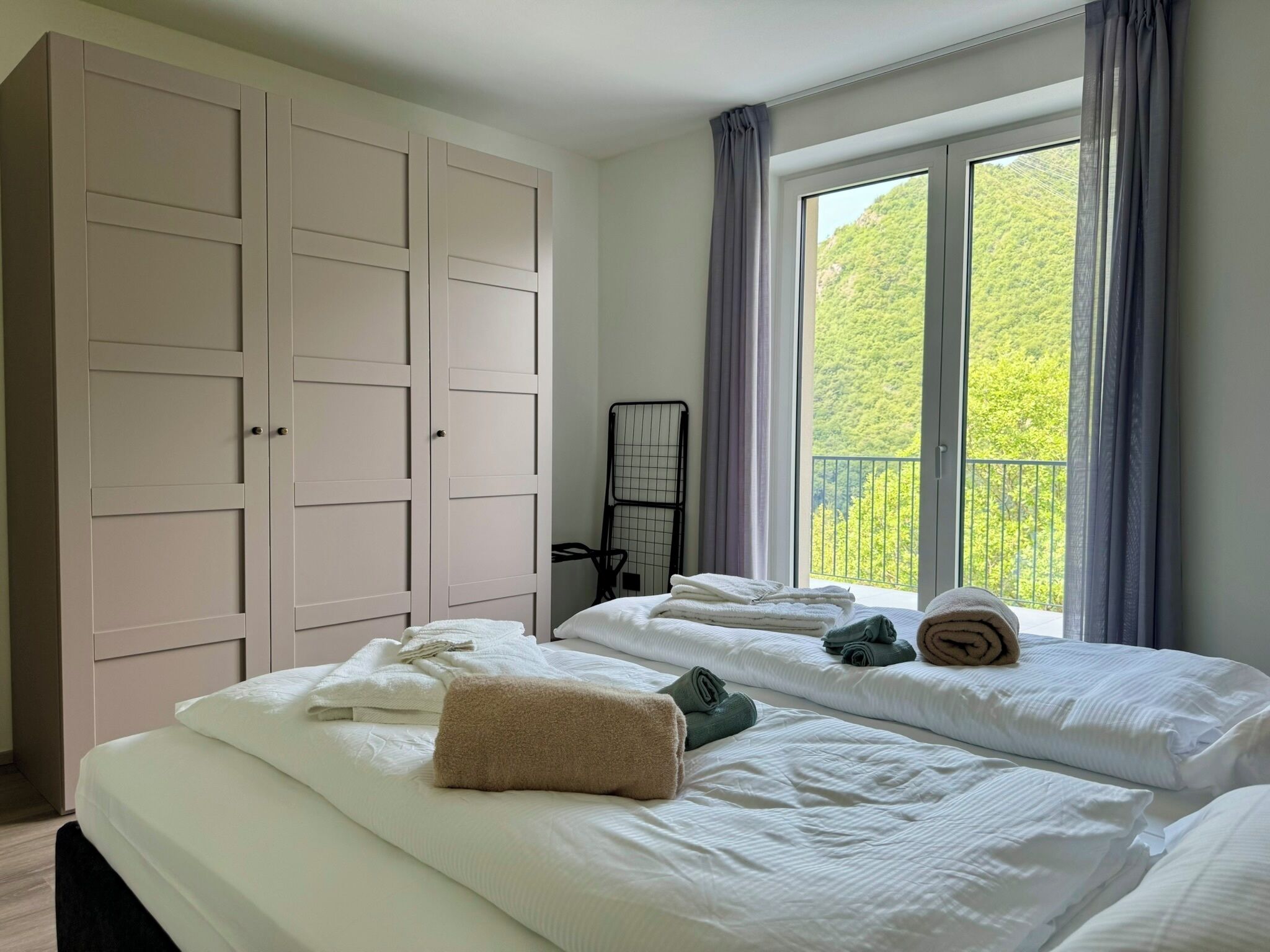 Ein Schlafzimmer mit zwei Betten, einem großen Kleiderschrank und einem Fenster mit Blick auf Grünflächen.