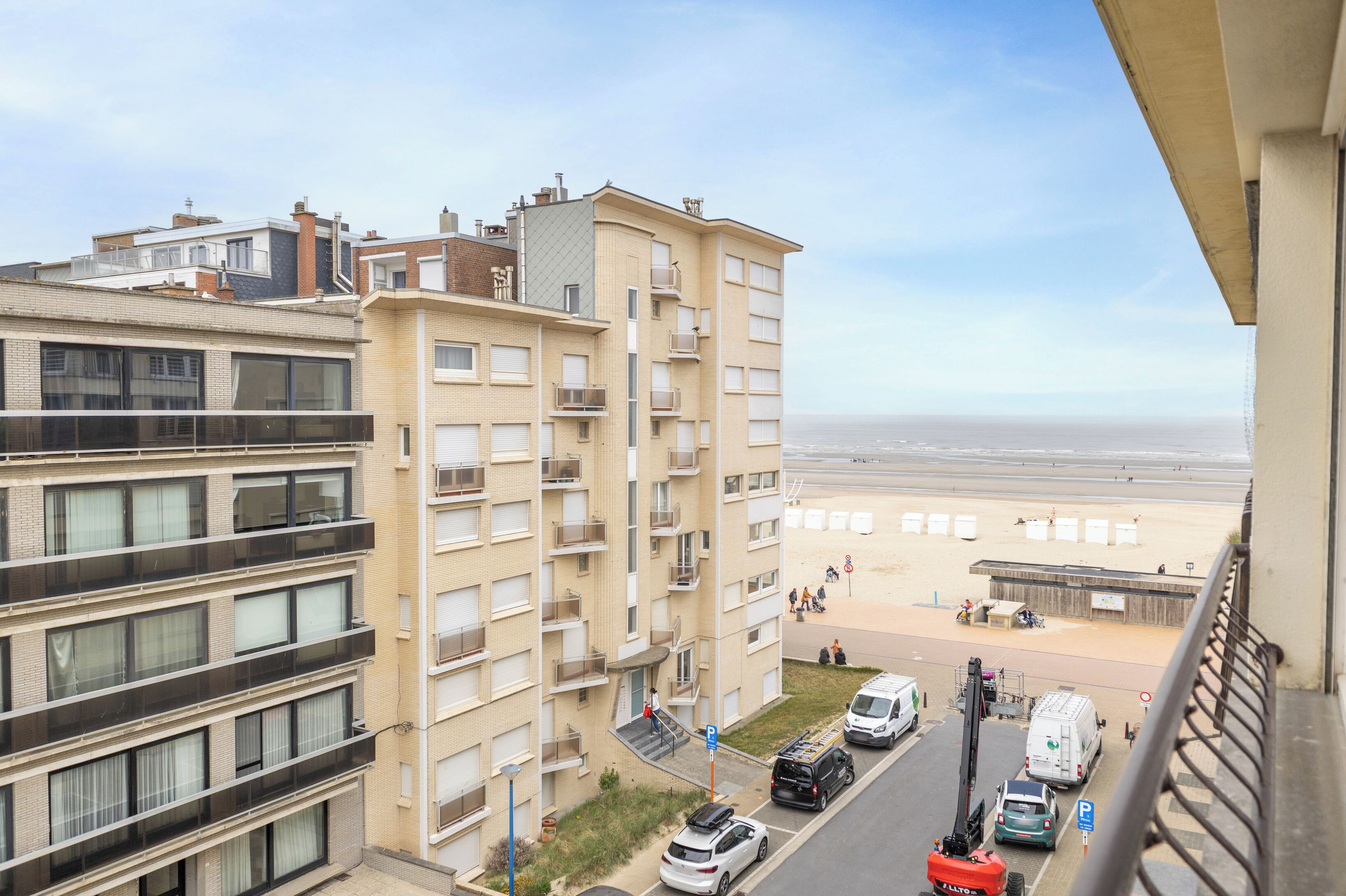 Un edificio de varios pisos con balcones, un estacionamiento y vista a la playa.