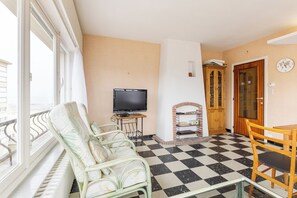Ein Zimmer mit Schachbrettfußboden, einem Fernseher, einer Holzkommode und einem Esstisch mit Stühlen.