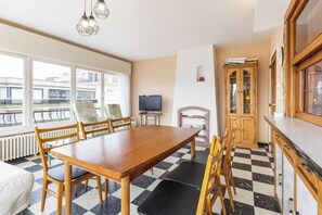 Ein Essbereich mit Holztisch und -stühlen, einem Fernseher und Blick ins Freie.