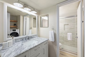 Une salle de bain avec un lavabo en marbre, deux miroirs, une cabine de douche en verre et des toilettes.