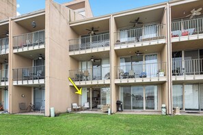 Un edificio residencial de varios pisos con balcones, mobiliario exterior y un jardín con césped.