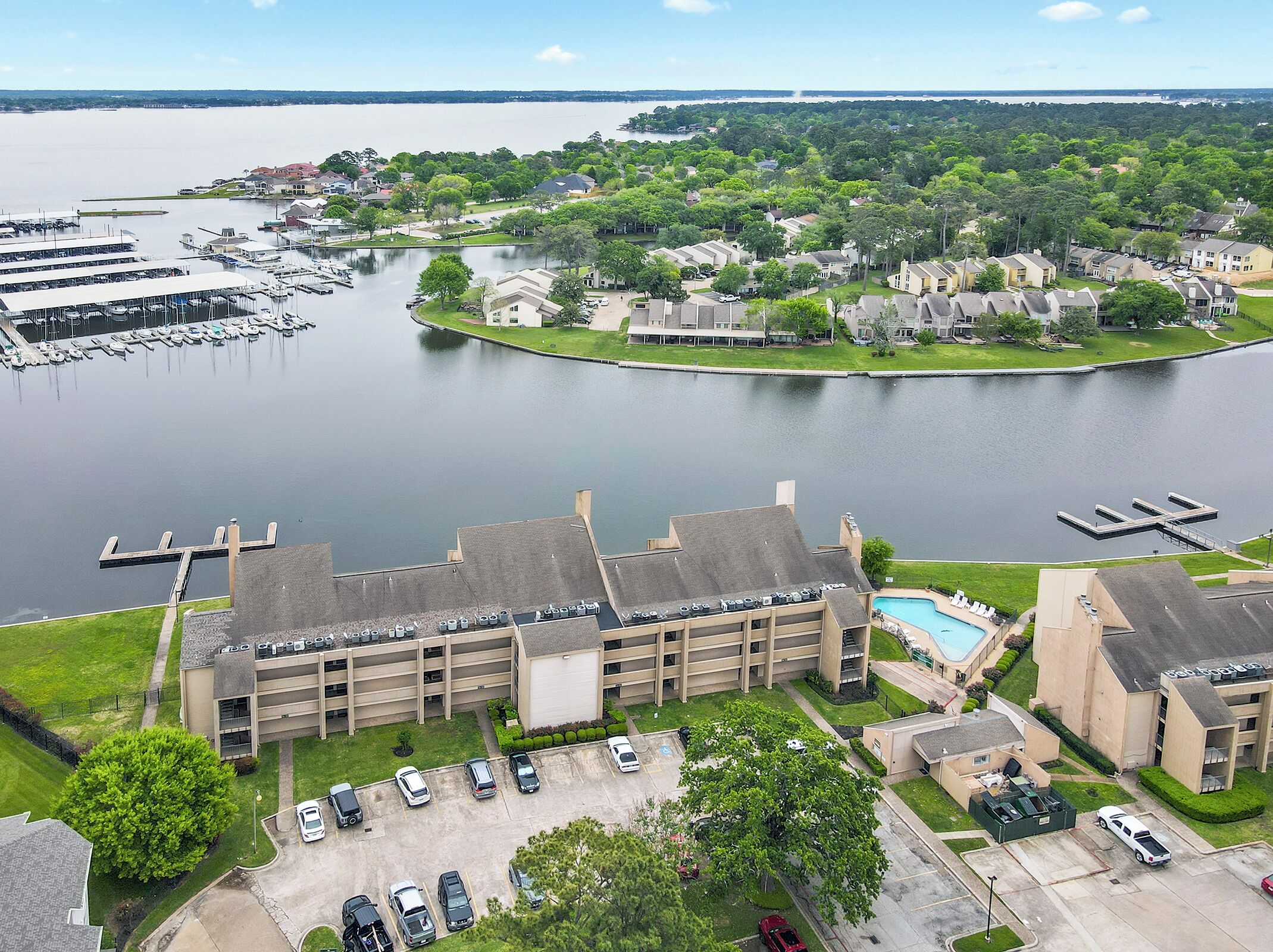 A multi-story building with a parking lot, a swimming pool, and a marina in the background.