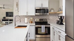 Una cocina moderna con armarios blancos, electrodomésticos de acero inoxidable, un microondas, horno y cafetera.