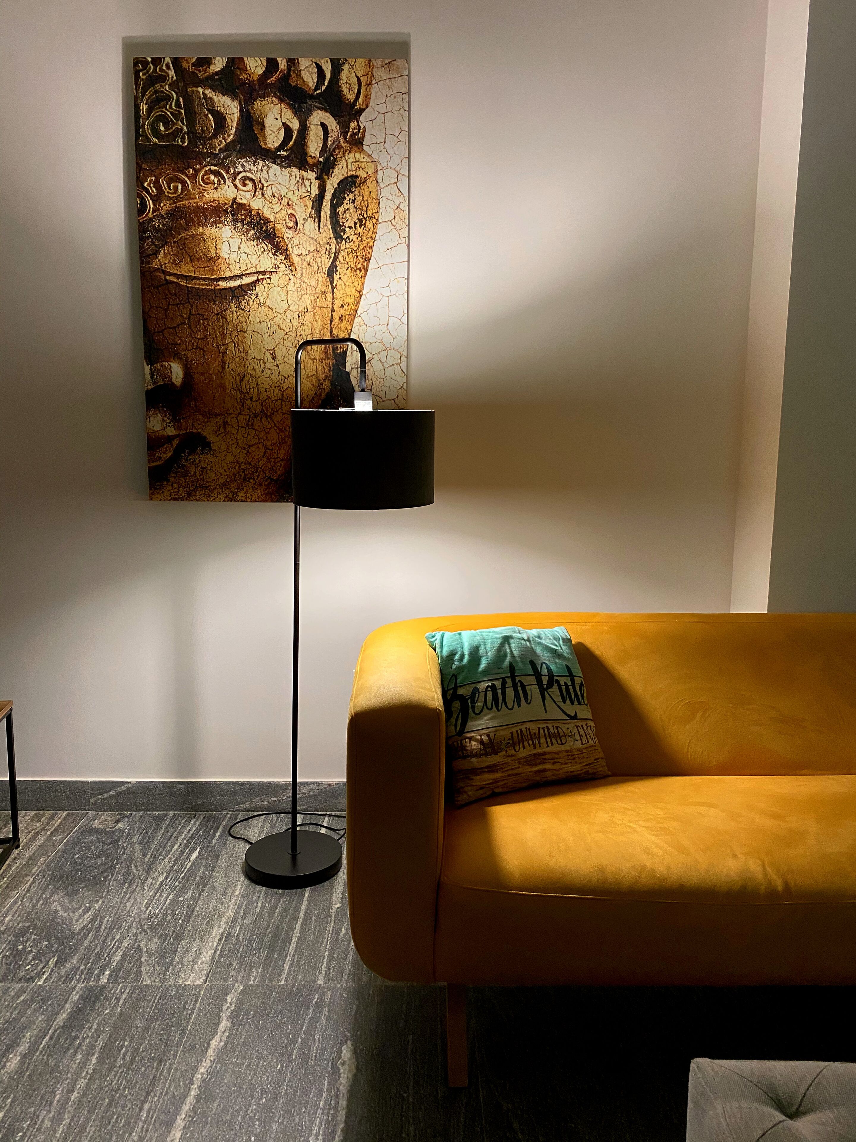 Una habitación con un sofá amarillo, una lámpara de pie negra y una obra de arte colgada en la pared.