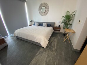 A modern bedroom with a large bed, a bedside table, a nightstand, a wall-mounted mirror, and a potted plant. - Spacious 3-bedroom apartment in beautiful Cancún with AC, Gym and rooftop Pool (Cancún)