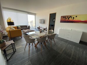A modern living room with a glass dining table, a sofa, and a painting on the wall. - Spacious 3-bedroom apartment in beautiful Cancún with AC, Gym and rooftop Pool (Cancún)