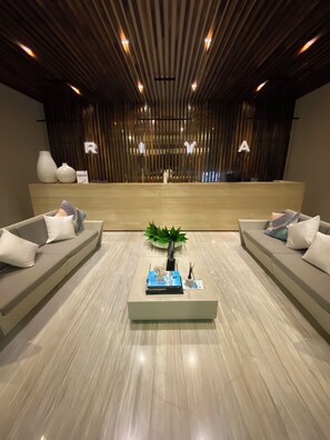 A reception area with a reception desk, two sofas with cushions, a coffee table with a plant, and a wooden slatted ceiling with lights. - Spacious 3-bedroom apartment in beautiful Cancún with AC, Gym and rooftop Pool (Cancún)