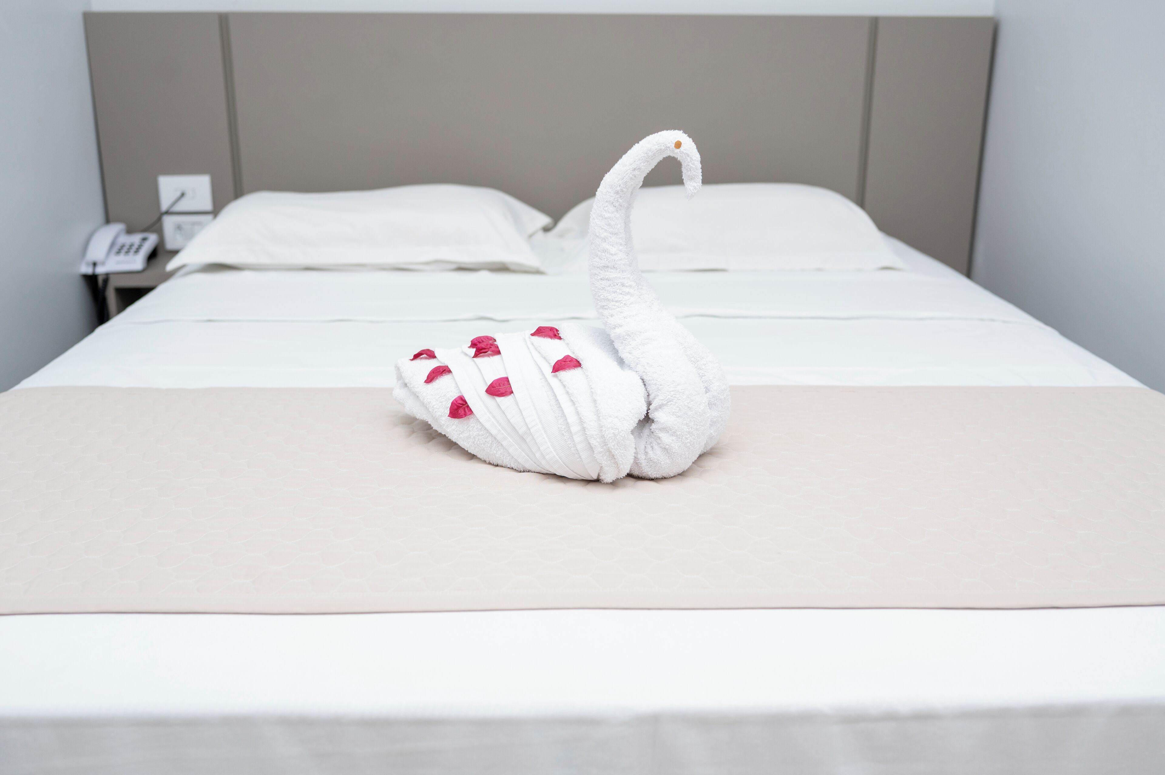 Cama bem arrumada com toalha em formato de cisne sobre o lençol.