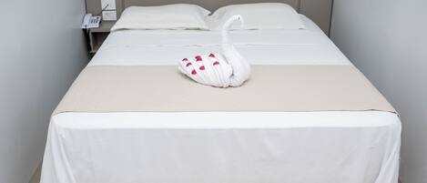 A neatly made bed with a swan-shaped pillow, a bedside phone, and a plain wall.
