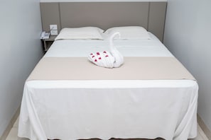 A neatly made bed with a swan-shaped pillow, a bedside phone, and a plain wall.