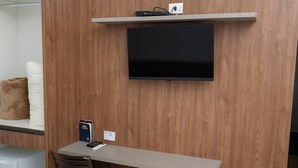 Habitación con televisión de pantalla plana montada en una pared de madera, un escritorio con una silla y un control remoto sobre el escritorio.