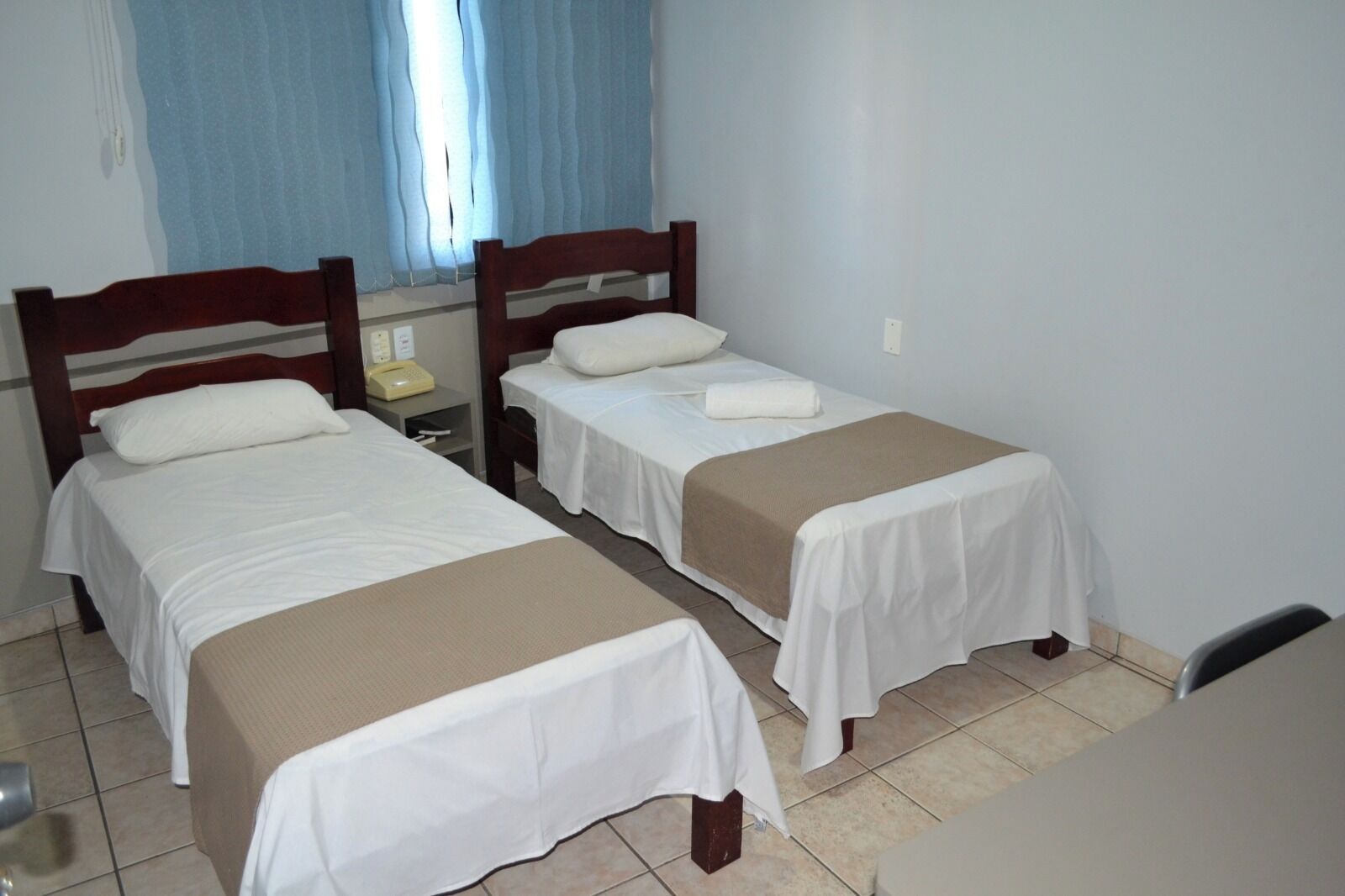 Quarto com duas camas de solteiro, mesa de cabeceira com telefone e janela com cortinas.