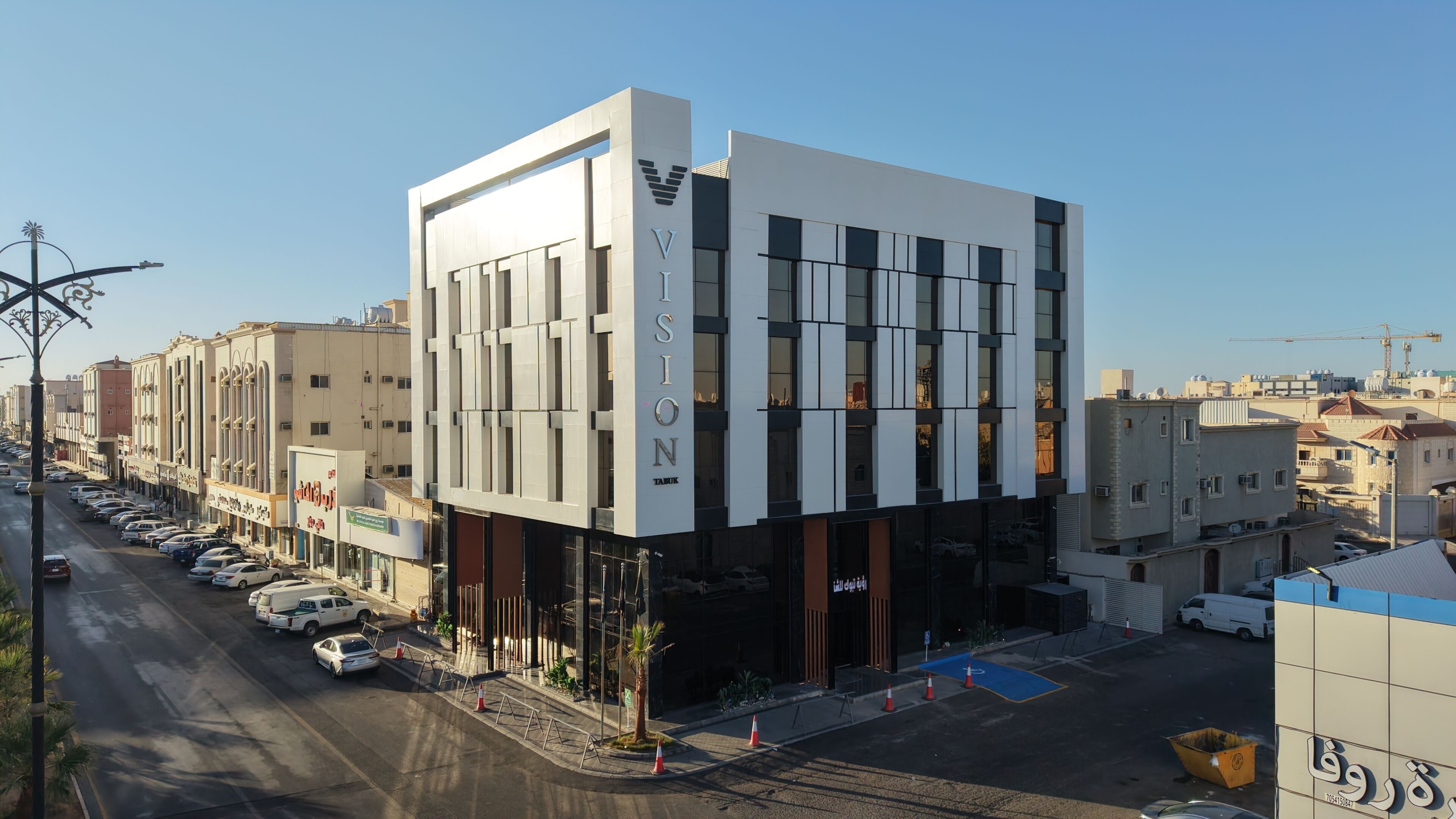 Um edifício moderno com um letreiro chamativo 'VISION', um estacionamento e edifícios urbanos ao redor.