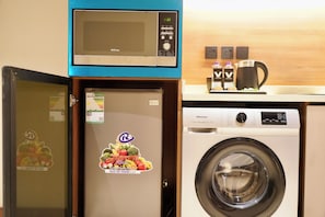 A compact kitchenette with a microwave, a refrigerator, and a washing machine. - VISION TABUK (TABUK)