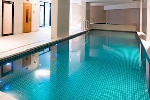 Ein überdachter Pool mit klarem Wasser, einer Leiter und einem gefliesten Boden.