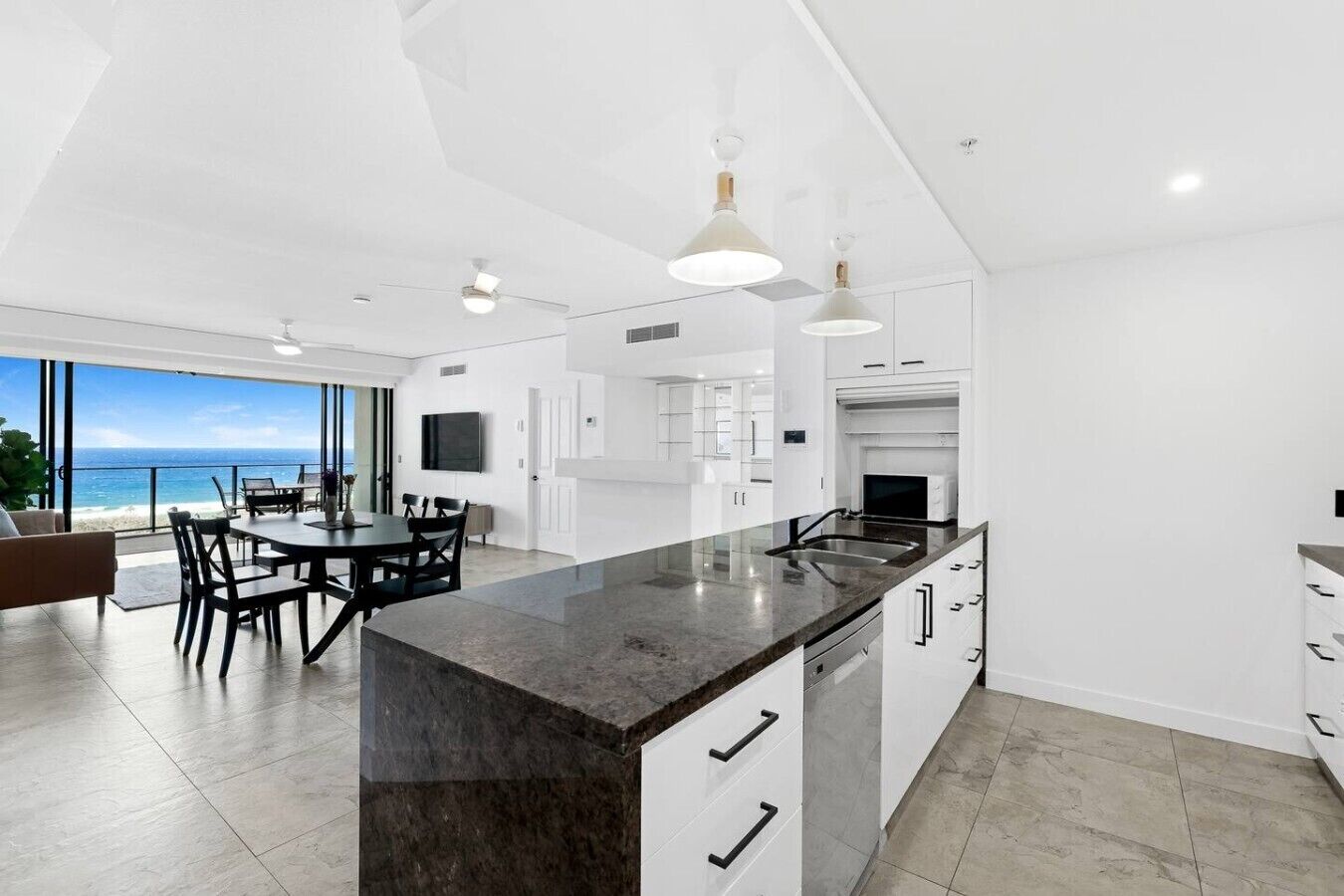 A modern kitchen with a large island, white cabinetry, and a view of the ocean.