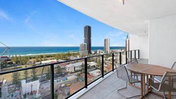 A balcony with a view of the ocean and cityscape, a table, and chairs.