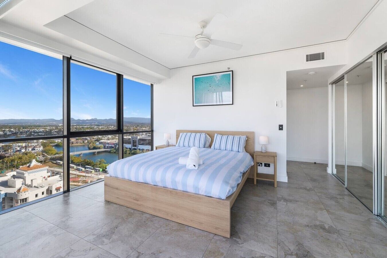 A modern bedroom with a large bed, a view of a cityscape, and a balcony.