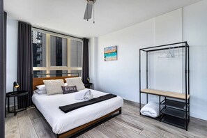 A modern hotel room with a large bed, a window with curtains, a painting, a black metal shelf, and a wooden bench. - Central 2B Apartment Parking. Wi-Fi. Views. (Surfers Paradise)
