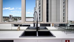 Ett modernt kök med ett stort fönster, en svart diskho och utsikt över en stadssiluett.