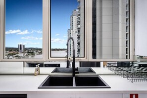 A modern kitchen with a large window, a black sink, and a view of a cityscape. - Central 2B Apartment Parking. Wi-Fi. Views. (Surfers Paradise)