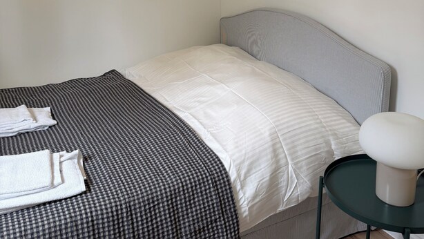 A small, neatly made bed with a striped headboard, a bedside table with a lamp, and a checkered blanket.
