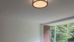 A modern bedroom with a large bed, a window with a view of a brick wall and greenery, and a table with chairs outside.