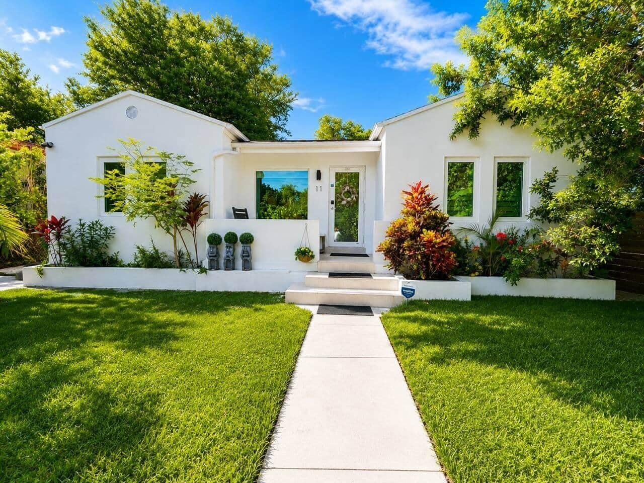 A two-story white house with a front porch, a clear sky, and well-maintained green lawns.