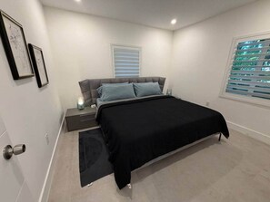 Ein Schlafzimmer mit Bett, Nachttisch, Lampe und einem Fenster mit Jalousien.