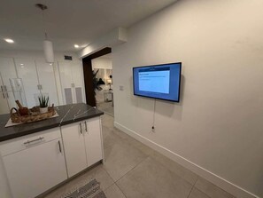 Eine moderne Küche mit weißen Schränken, einer Marmorarbeitsplatte und einem flachbildfernseher an der Wand.