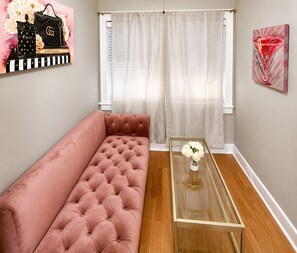 Ein Wohnzimmer mit einem rosafarbenen Sofa, einem Glastisch mit Blumen und einem Gemälde von einem Cocktailglas.