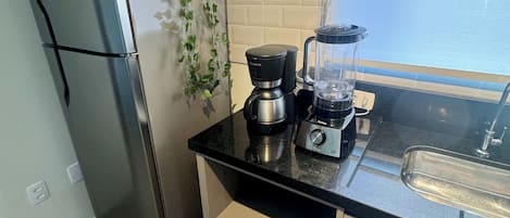 Una cocina compacta con un refrigerador de acero inoxidable, una cafetera, una licuadora y un ventanal con vistas.