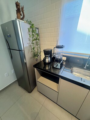 Eine kleine Küche mit einem Edelstahlkühlschrank, einer Kaffeemaschine, einem Mixer und einem Fenster mit Blick.