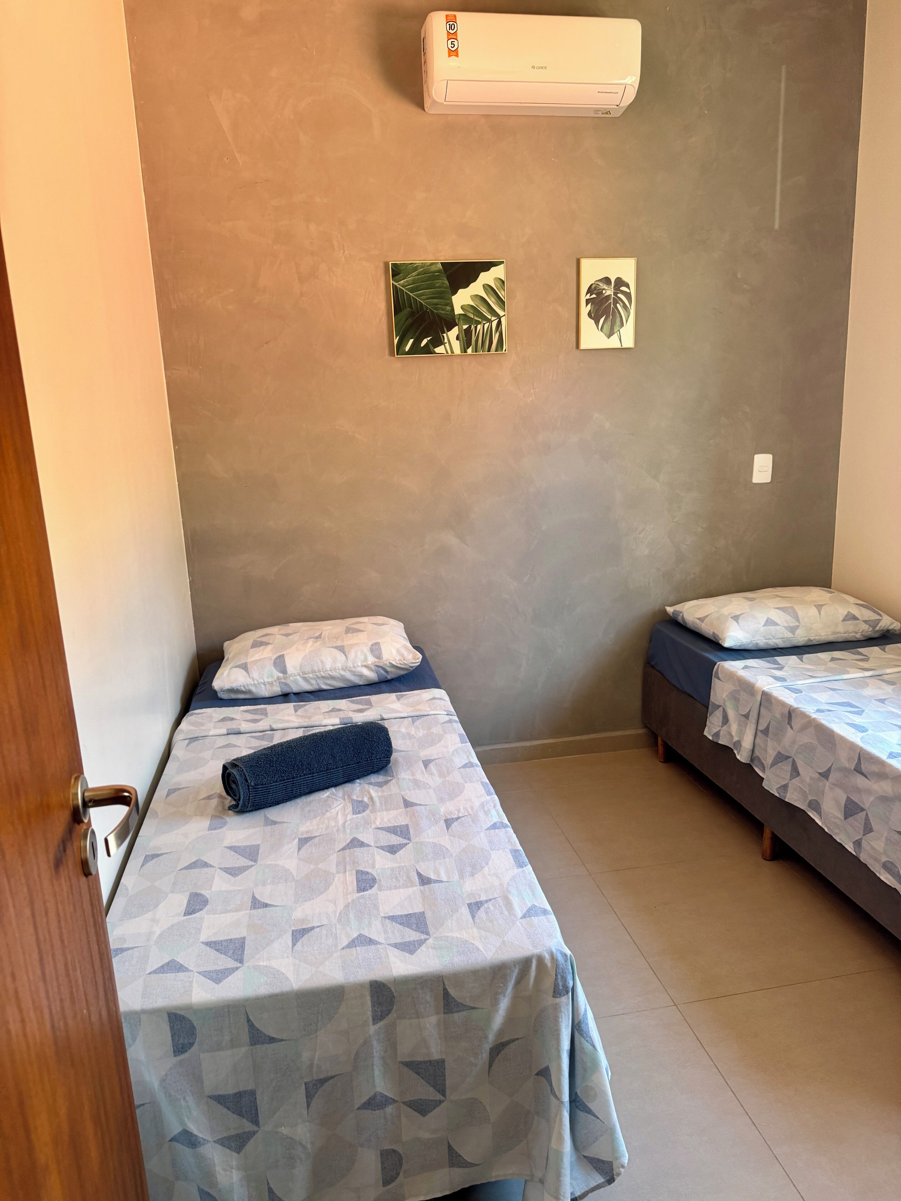 Une chambre avec deux lits, un climatiseur fixé au mur et deux tableaux encadrés.