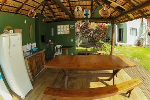 A covered outdoor dining area with a wooden table and benches, a refrigerator, and a small kitchen area with a sink and cabinets. - New and comfortable apartment near the beach and everything, with air conditioning. (Florianópolis)