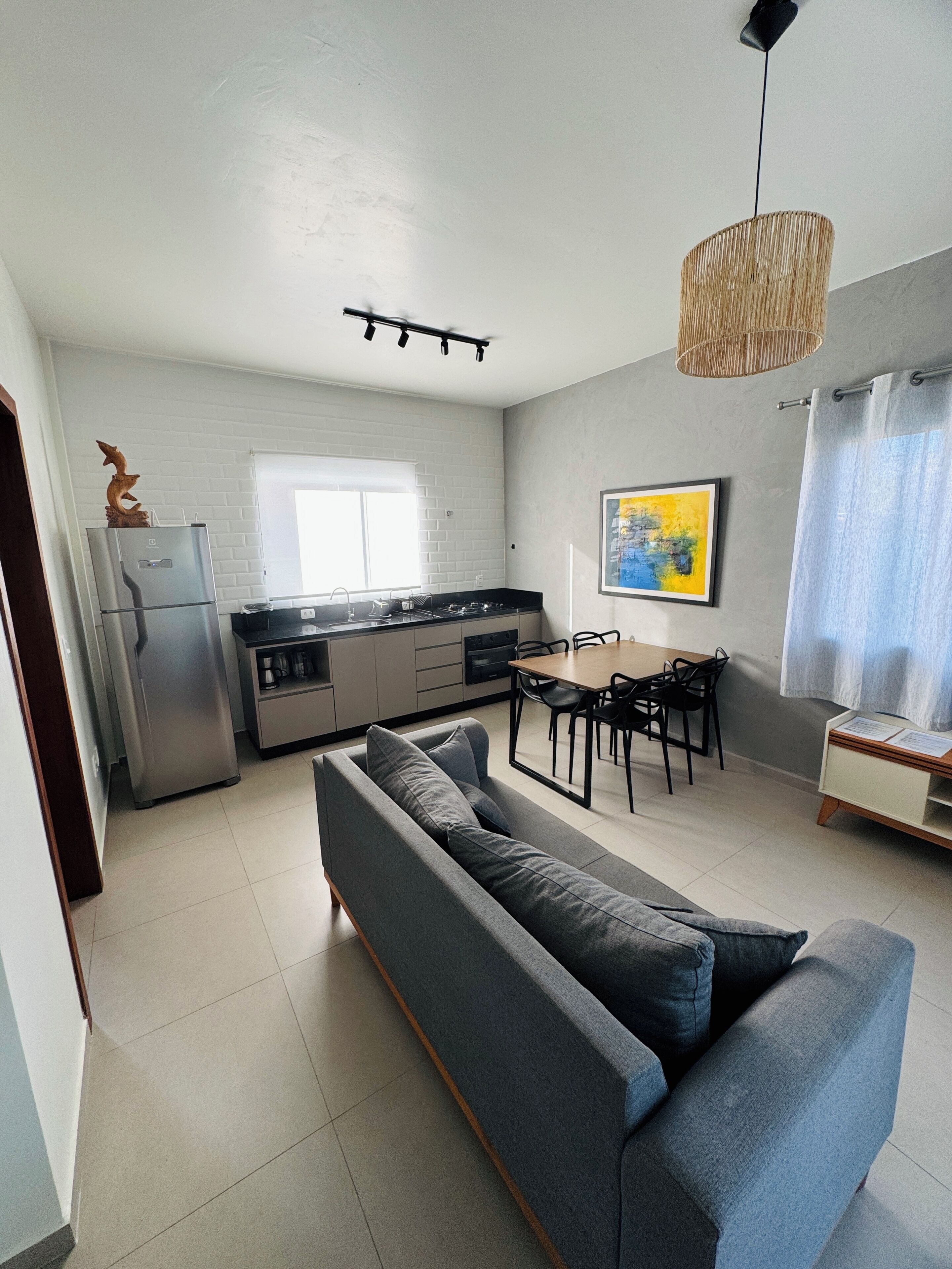A modern kitchen with a built-in oven, a dining area with a table and chairs, and a grey sofa in the living room.
