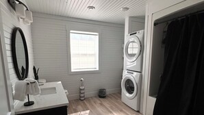 A modern bathroom with a sink, mirror, and two stacked washing machines. - Country Acres Cottages Cottage #3 central to North Rustico and Cavendish, PE. (North Rustico)