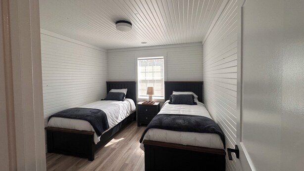 A bedroom with two beds, wooden flooring, a window, and a ceiling vent. - Country Acres Cottages Cottage #3 central to North Rustico and Cavendish, PE. (North Rustico)
