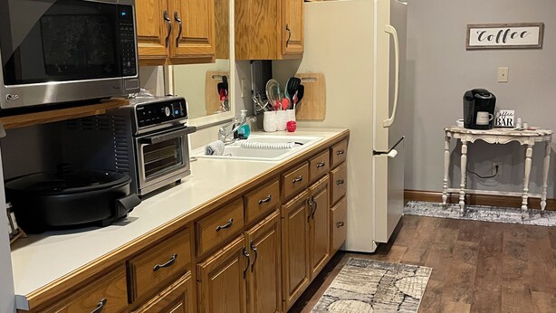 Una cocina con armarios de madera, microondas, horno, refrigerador y una zona para café.