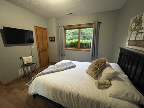 A bedroom with a bed, a television mounted on the wall, a window with curtains, and a door. - IU F'ball 2 BDR lower level apartment with private entrance in Bloomington, IN (Bloomington)