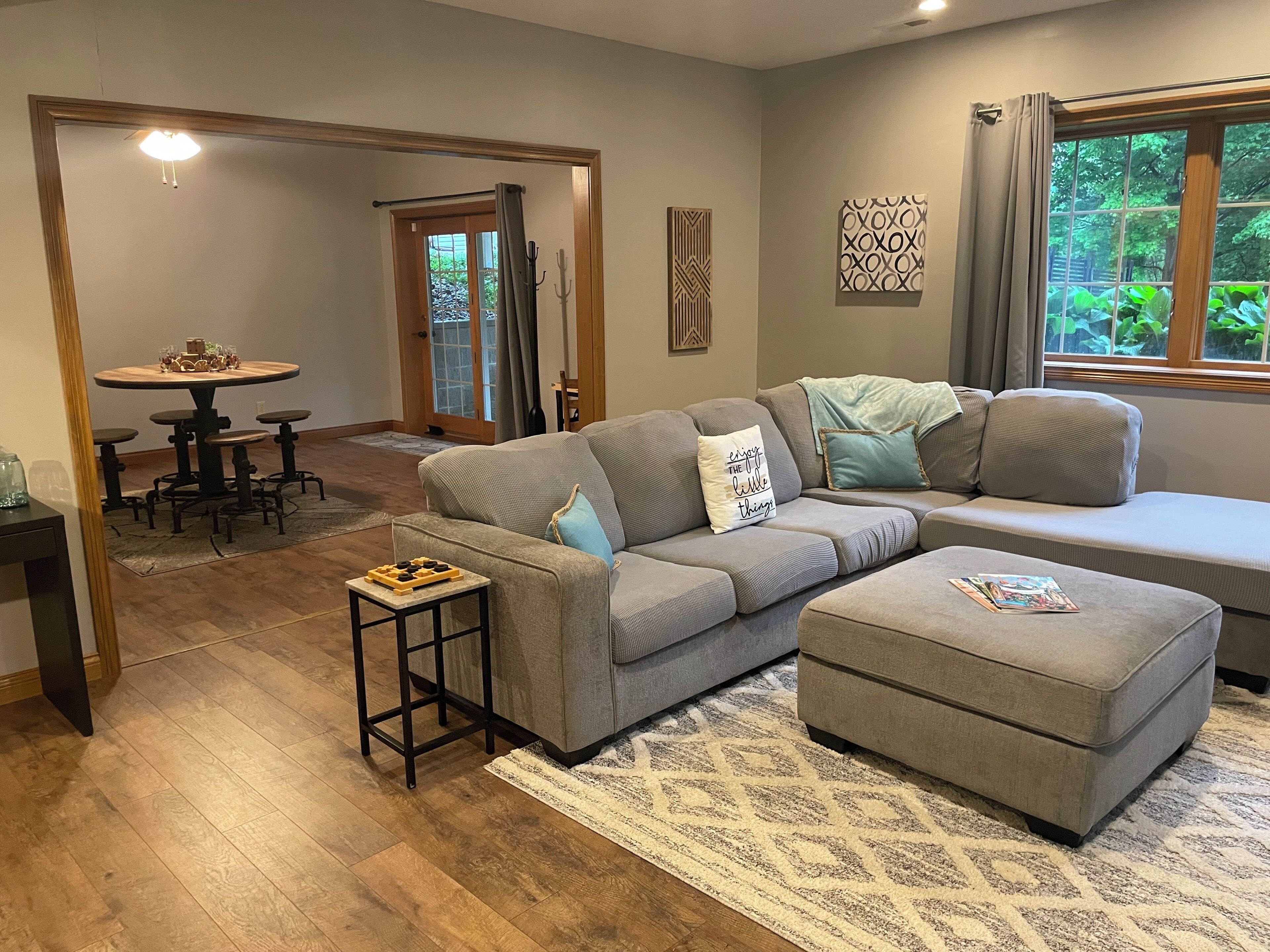A living room with a sectional sofa, ottoman, coffee table, and a dining area with a round table and chairs.